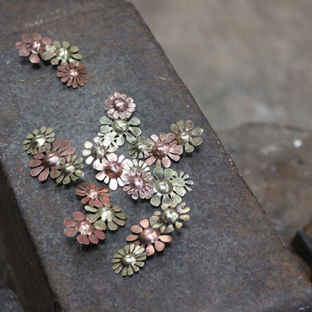 Boucle d'oreille Marguerites en cuivre laiton et argent, fabriquées artisanalement par les Métalleuses en fusion, photo sur l'enclume.