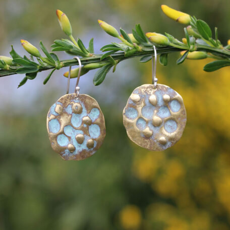 Boucles d'oreilles terre de lune en laiton, patine vert de gris et attaches en argent. Fabriquées artisanalement par les métallleuses en fusion. Vue suspendues.