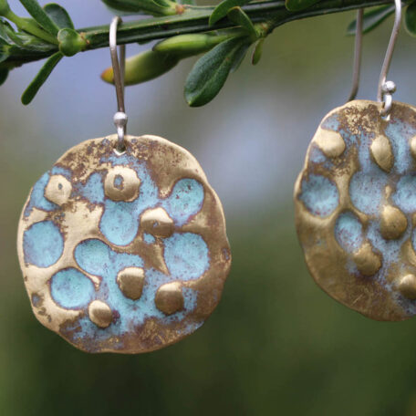 Boucles d'oreilles terre de lune en laiton, patine vert de gris et attaches en argent. Fabriquées artisanalement par les métallleuses en fusion. Vue rapprochée.