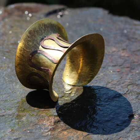 Bracelets del Sole en laiton, fabriqués artisanalement avec la technique de la dinanderie par les métalleuses en fusion.  Vue sur une ardoise.